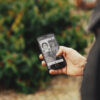 A man is holding a smartphone. On the screen is a portrait of a woman