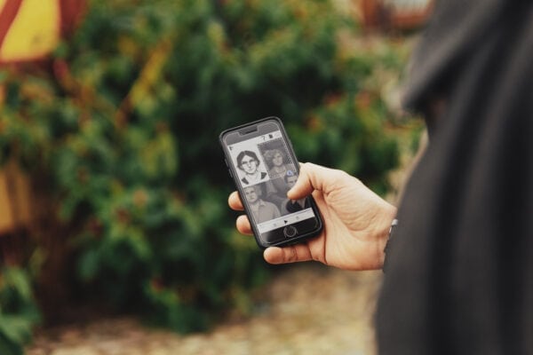 A man is holding a smartphone. On the screen is a portrait of a woman