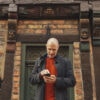 A man is standing in front of a half-timbred house. He is looking at his phone