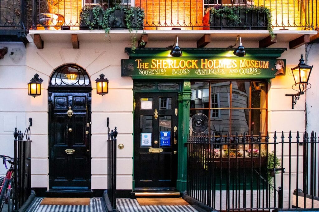 An exterior picture of 221B Baker street with a black door and the windows of the museum next to it.