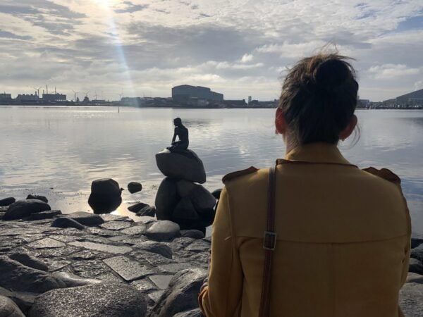 A woman in a yellow coat is looking at The Little Mermaid statue