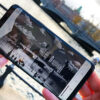 A woman is holding a smartphone, an old black and white photo is visible on the screen