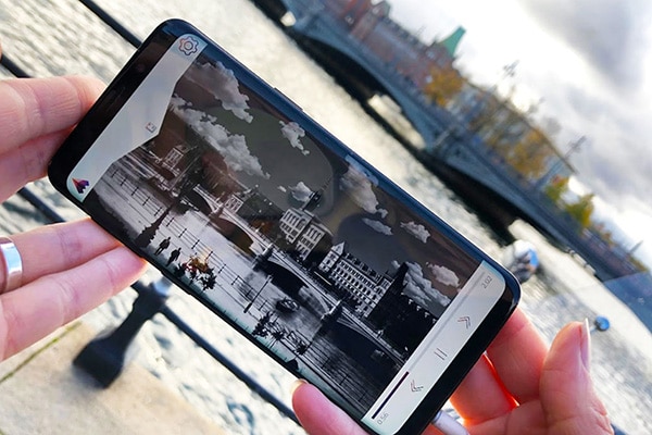 A woman is holding a smartphone, an old black and white photo is visible on the screen