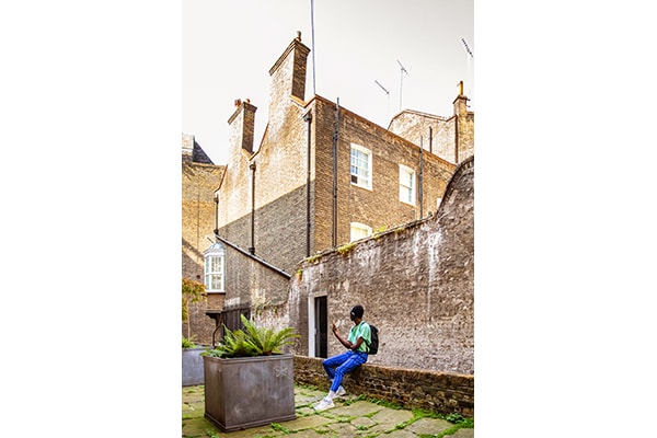 A young man is sitting on a brick wall in an alley