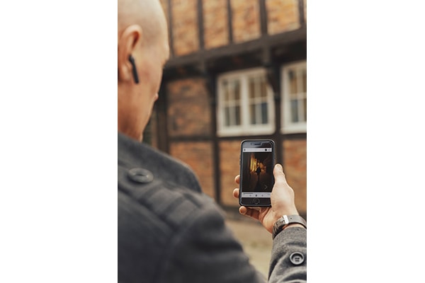 A man standing in front of a half timbred house is holding up his smartphone