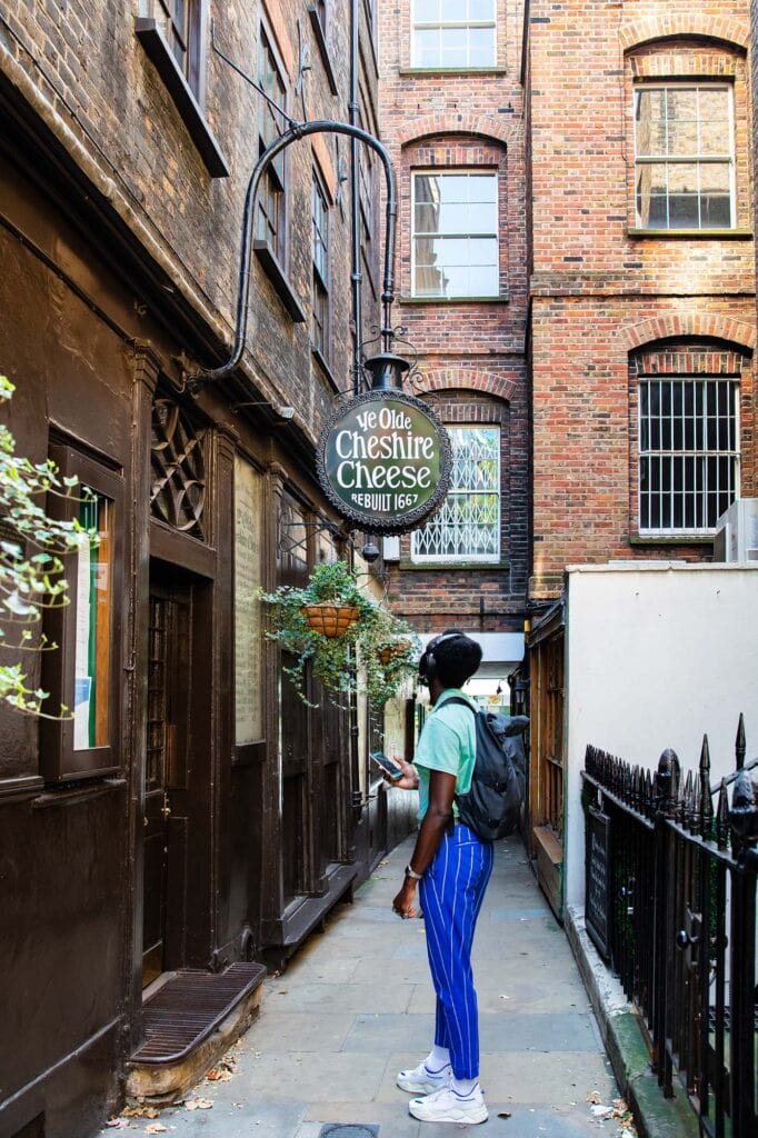 A young man is standing in an alley looking up at the sign of Ye Olde Cheshire Cheese