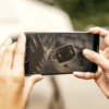 A woman's hands are holding a smartphone. On the screen is an image of old items strewn about in a prison cell.