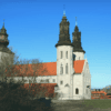 A photograpgh of Sankta Maria cathedral taken from a distance. The church is white with dark colored spires. The sky is very blue.