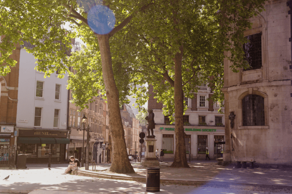 A man is sitting on the curb outside St Clement Danes Church, eating his lunch. It's a sunny day.