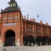 A facade image of the food market at Östermalm in Stockholm. A big, red, brick building with an arched entryway.
