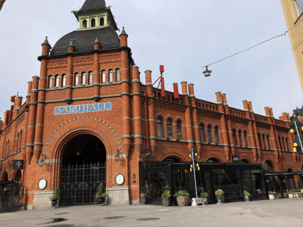A facade image of the food market at Östermalm in Stockholm. A big, red, brick building with an arched entryway.